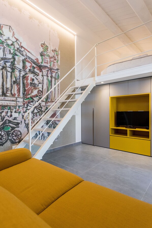 A modern living room with a staircase, a yellow sofa, and a mural on the wall.