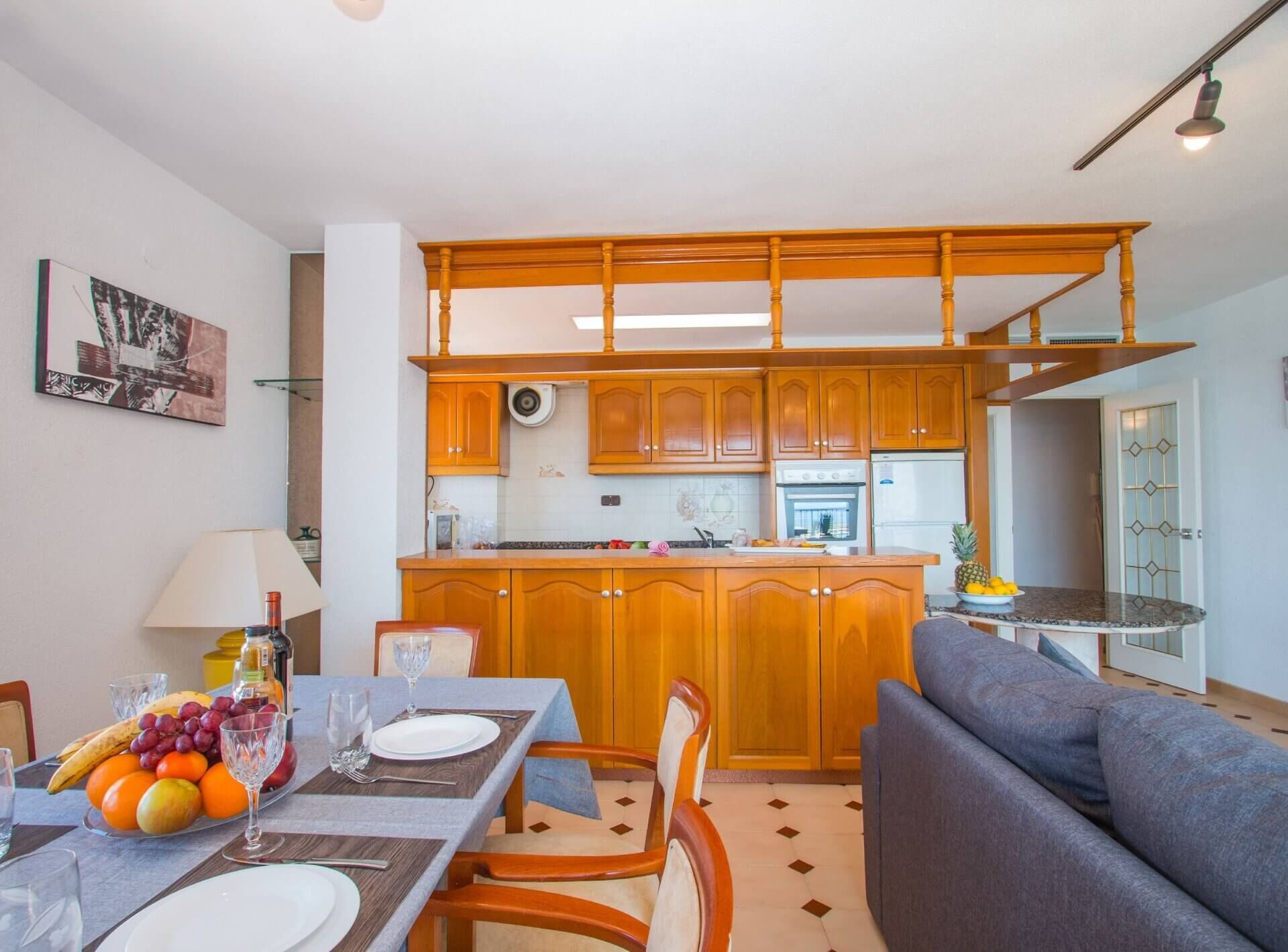 Una cocina moderna con armarios de madera, una isla central y un comedor con una mesa dispuesta para dos personas.