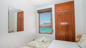 Quarto com cama, janela com vista para o mar, guarda-roupa de madeira e espelho.