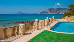 Uma área de piscina com vista para o mar e uma montanha ao longe.