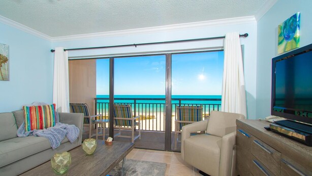 A balcony with a view of the ocean, a sofa, a coffee table, and a TV.