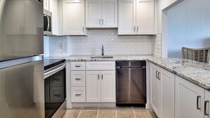 A modern kitchen with white cabinets, stainless steel appliances, and a tiled backsplash.