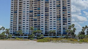 A high-rise building with multiple balconies, surrounded by palm trees and a clear sky.