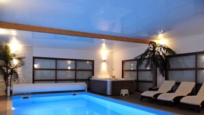 Ein Pool mit einer eingelassenen Sitzecke, einem Massagetisch und Liegestühlen.