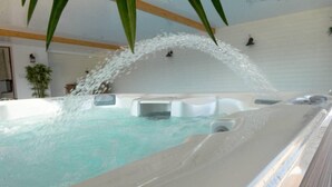 Ein Whirlpool mit Wasserstrahlen, umgeben von einer weißen Mauer und Holzbalken.