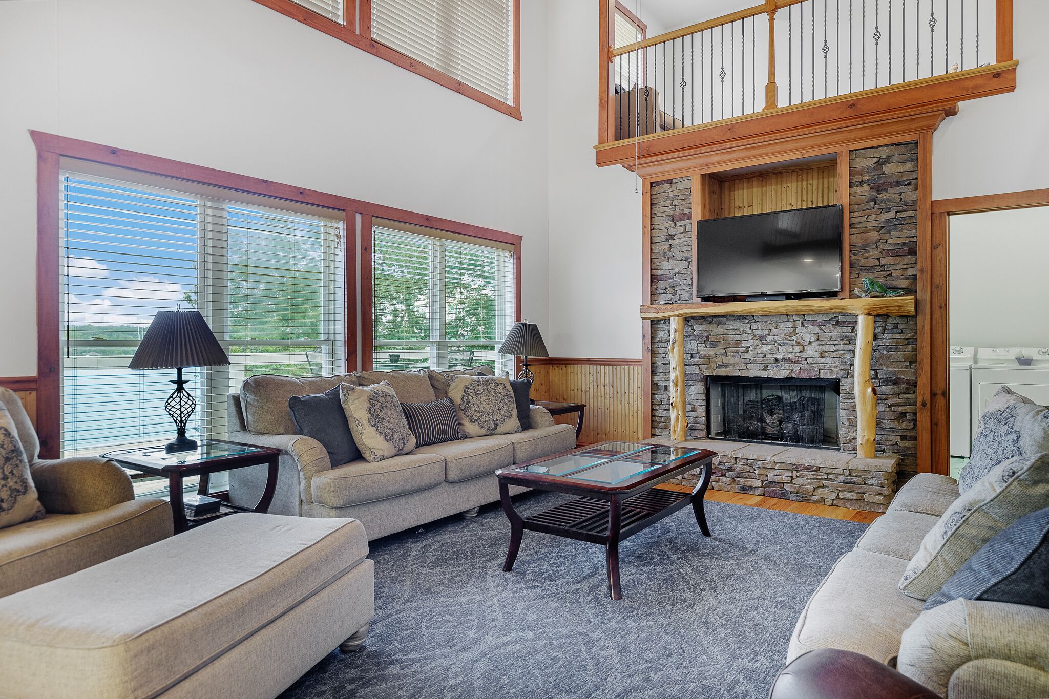 A spacious living room with a stone fireplace, a large flat-screen TV mounted above it, and a comfortable seating area with a sofa and two armchairs.