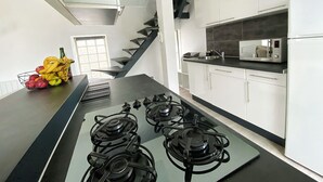 Une cuisine moderne dotée d’un îlot central, d’une cuisinière à gaz, d’un four à micro-ondes et de meubles de couleur blanche.