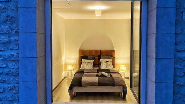 Une chambre d’hôtel avec un lit, deux lampes de chevet et une vue sur l’extérieur, visible à travers une porte vitrée.