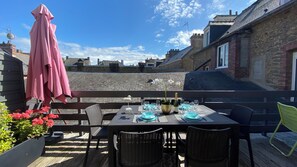 A patio with a table set for dining, surrounded by wicker chairs and a pink umbrella. - Cézembre apartment 150 m from the lock beach (Dinard)