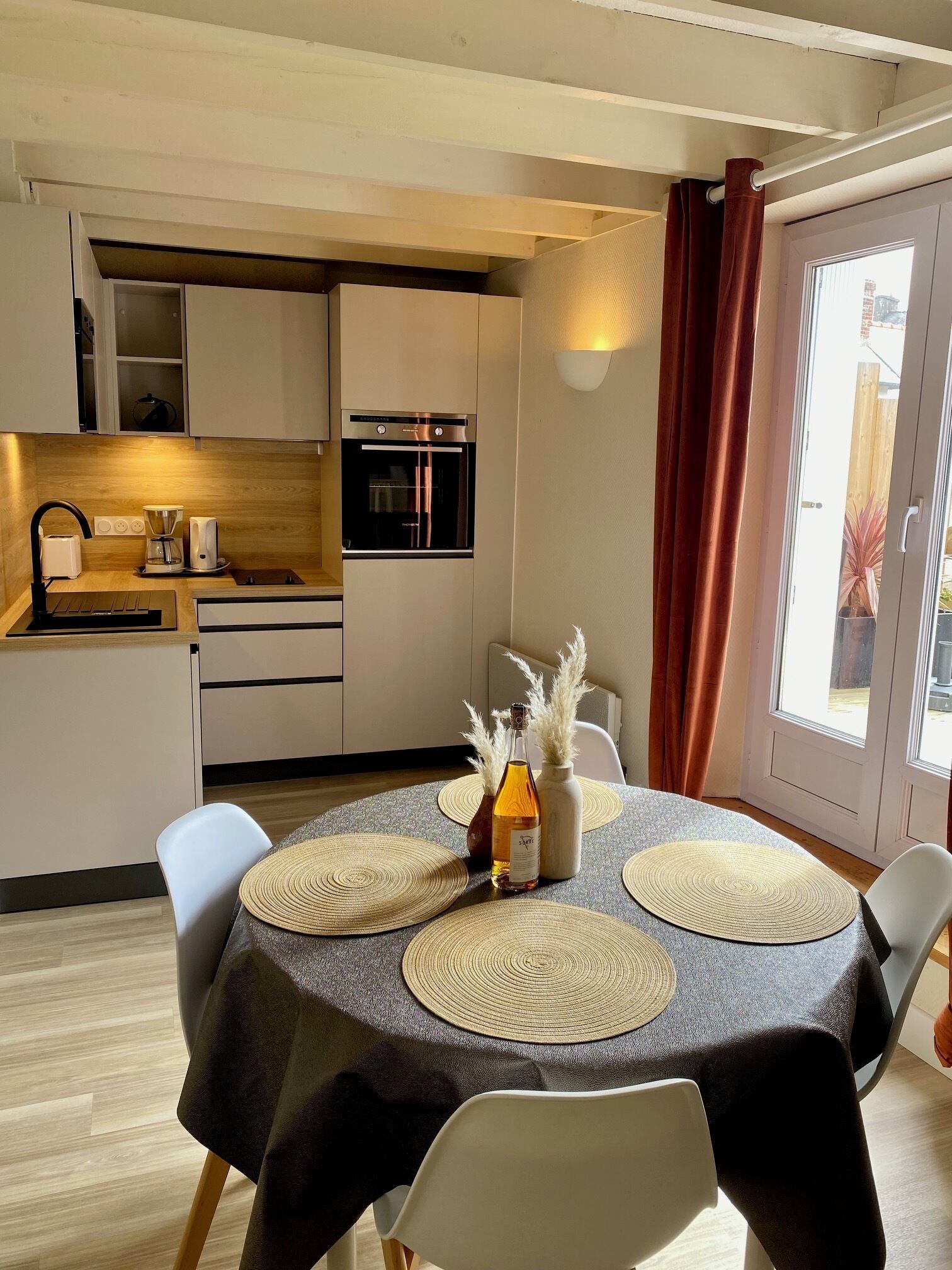 A compact kitchen with modern appliances, a dining area with a round table and chairs, and a view through a sliding door.