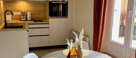 A compact kitchen with modern appliances, a dining area with a round table and chairs, and a view through a sliding door.