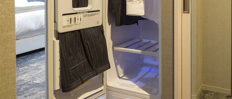 A hotel room with a walk-in closet containing a hanging rack, a folded towel, and a shelf.