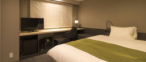 A hotel room with a bed, a desk with a computer, a television, and a lamp.