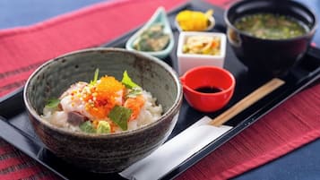 Un bol de sushi con ingredientes, acompañado de pequeños recipientes de salsas y un tazón de sopa en una bandeja.