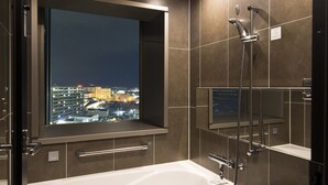A modern bathroom with a bathtub, a shower, and a window with a city view.