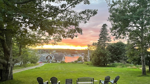 A grassy area with outdoor seating and a view of a lake and buildings in the distance. - Spacious Cottage Overlooking Bass Harbor with Sweeping Front Lawn (Bass Harbor)