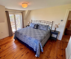 Un dormitorio con cama, mesita de noche, lámpara, ventana con cortinas y puerta.
