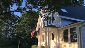 A two-story house with a porch, a flag, and a well-maintained lawn. - Spacious Cottage Overlooking Bass Harbor with Sweeping Front Lawn (Bass Harbor)
