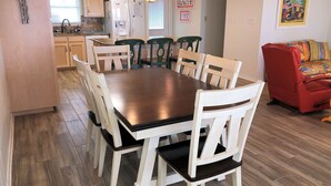 A dining area with a wooden table and white chairs, a kitchen with light wooden cabinets, and a red sofa in the living area. - Sunset Key - Soundfront with Boat Dock, 3 Bedrooms, 2 Baths, Sleeps 9. (Dauphin Island)