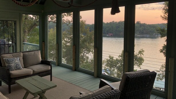 Une véranda aménagée avec des meubles en osier, de grandes fenêtres et une vue sur un lac.