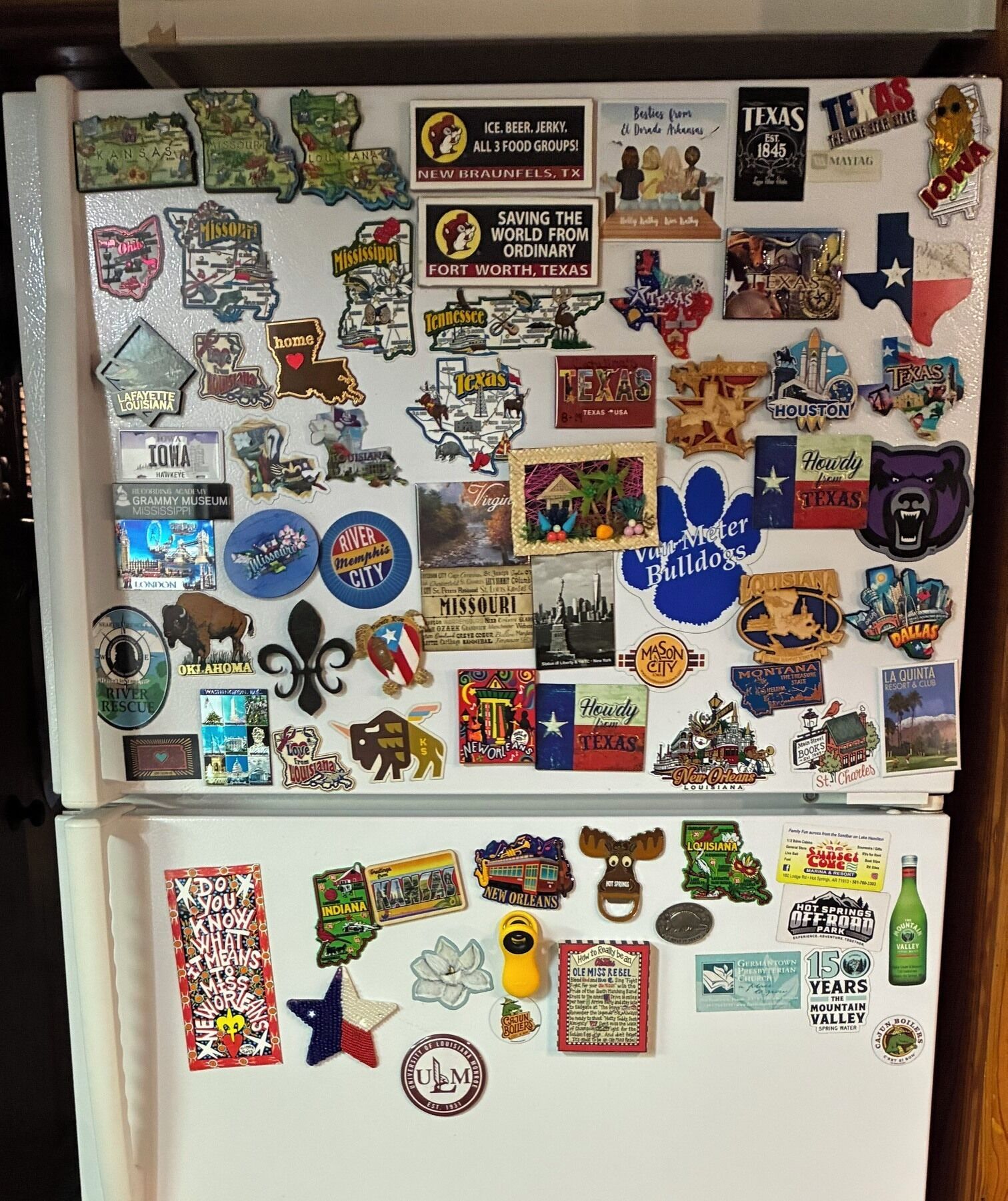 Een koelkast beplakt met diverse stickers en magneten, waaronder staatswapens, logo's en tekst.