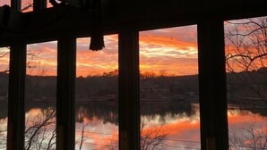 Une pièce dotée de grandes fenêtres donnant sur un plan d’eau et offrant une vue sur le coucher de soleil.