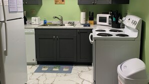 Cocina compacta con armarios oscuros, un refrigerador blanco, microondas, estufa y un bote de basura.