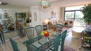 A dining area with a glass table, green chairs, and a fruit bowl.