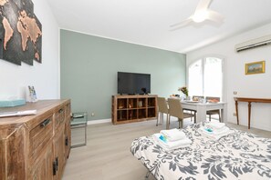Camera d'albergo con un letto, una cassettiera in legno, una televisione, una scrivania con una sedia e un'ampia finestra.