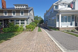 Una calle residencial con casas de dos pisos, un sendero de ladrillo y una valla de madera.