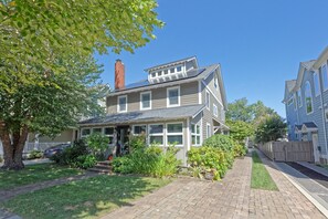A two-story house with a front porch, a chimney, and a brick pathway leading to the entrance.