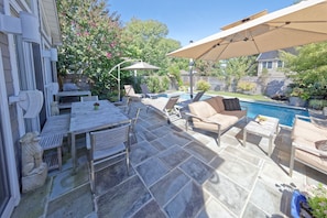 Eine Außenpatio mit Pool, Steinböden und Gartenmöbeln, darunter ein Tisch, Stühle und eine Sitzecke.