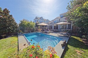 A backyard with a swimming pool, patio furniture, and a house in the background.