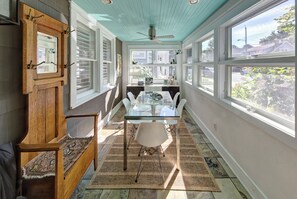 Un coin repas lumineux, avec une table en verre, des chaises blanches et un ventilateur de plafond.