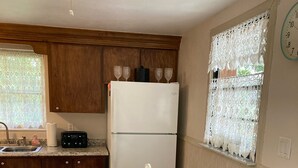 A kitchen with a white refrigerator, wooden cabinets, a sink, and a dining table with green placemats and wooden chairs. - CHARLOTTE HARBOR BUNGALOW (Port Charlotte)