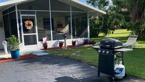 A covered porch with a grill and propane tank, potted plants, and a wreath on the door. - CHARLOTTE HARBOR BUNGALOW (Port Charlotte)