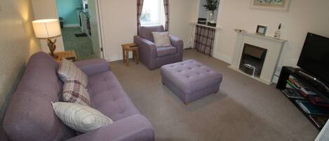 A living room with a purple sofa, a matching ottoman, a television, and a fireplace.