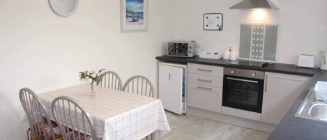 A compact kitchen with a dining area, featuring a tiled backsplash, a built-in oven, a microwave, and a small refrigerator.
