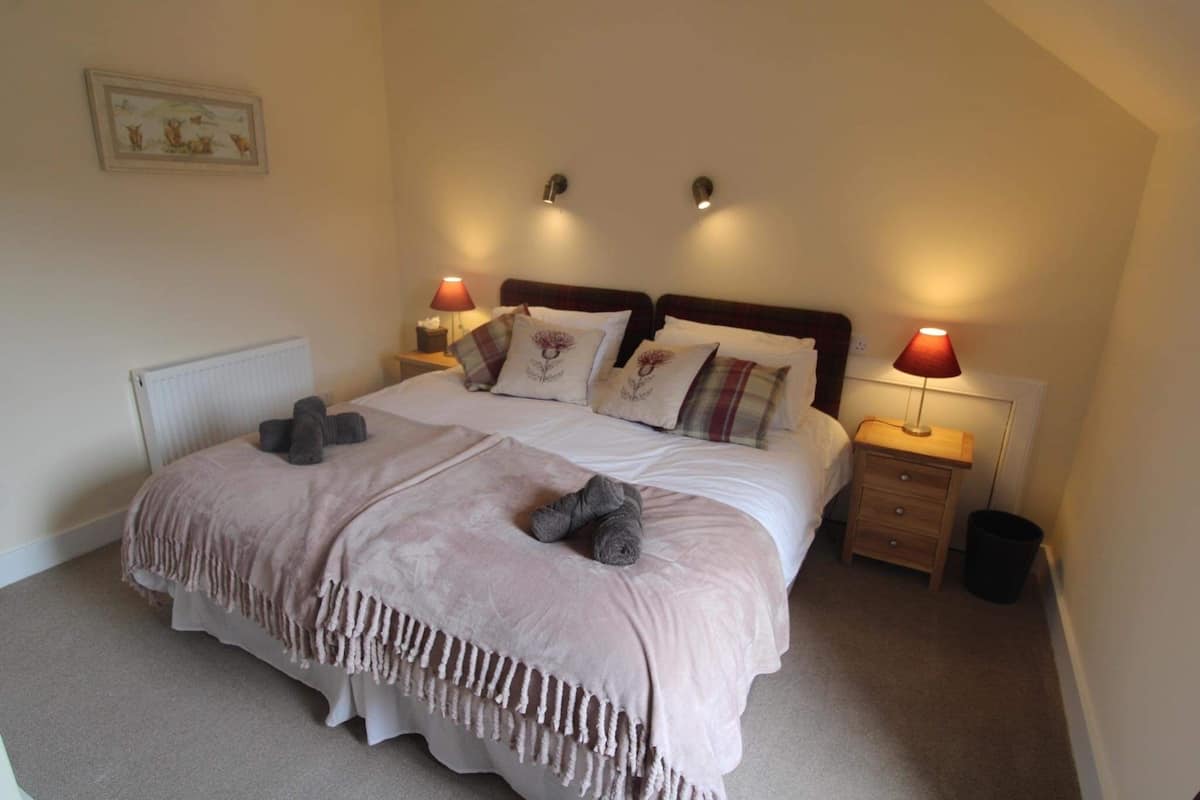 A neatly made bed with a blanket and pillows, two bedside lamps, a small bedside table, and a radiator.