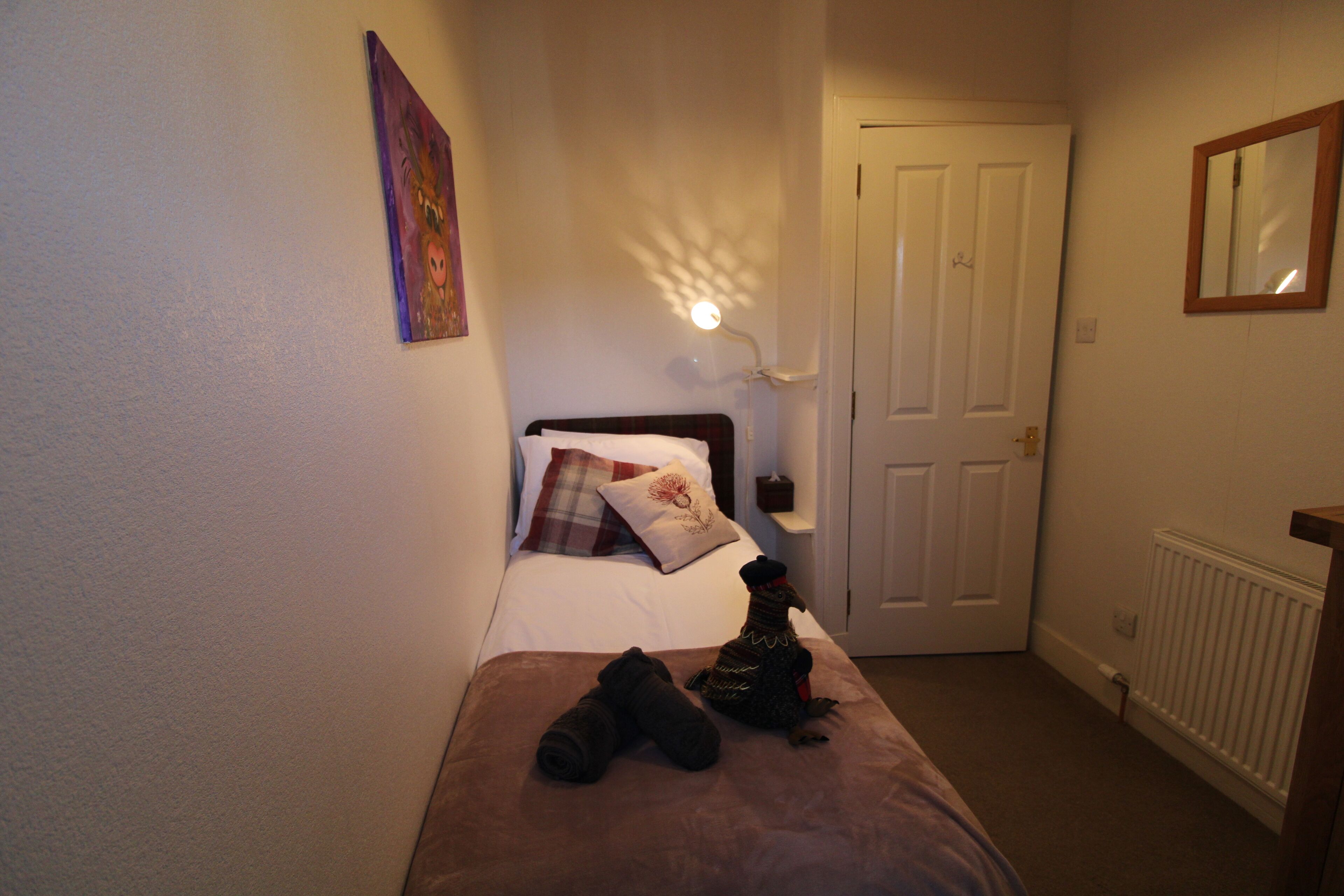 A bedroom with a bed, a nightstand, a lamp, a door, and a radiator.