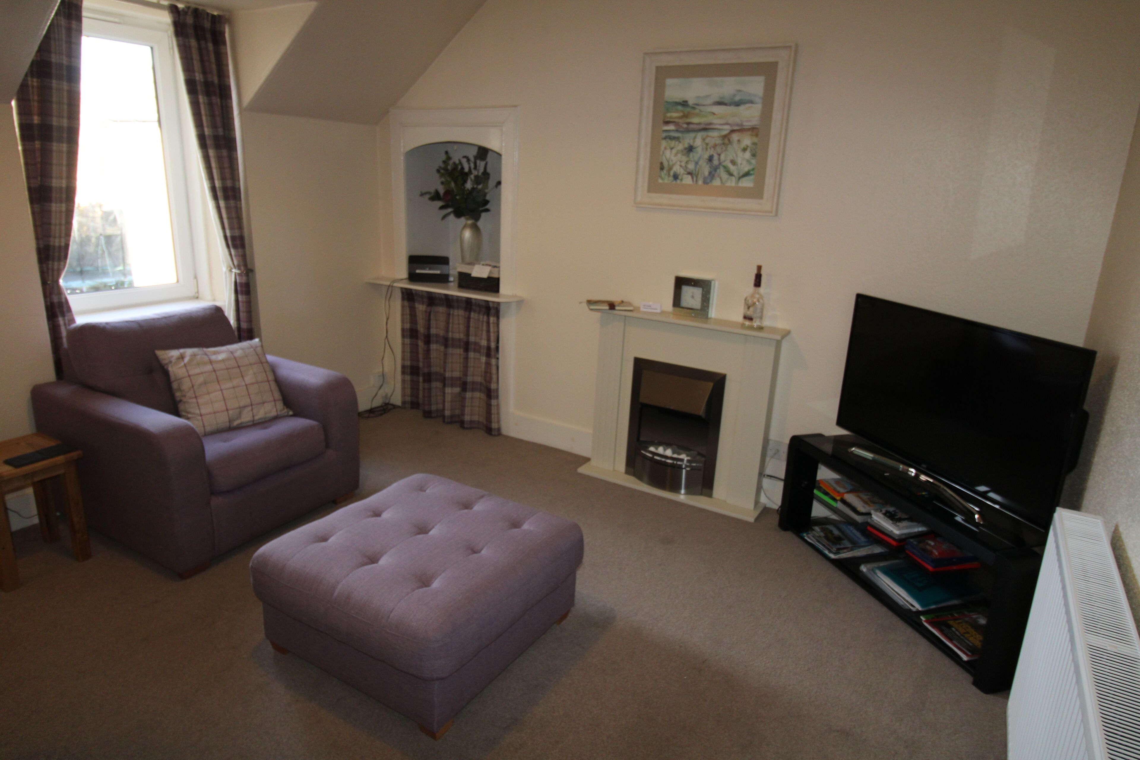 A living room with a sofa, ottoman, fireplace, TV, and a bookshelf.