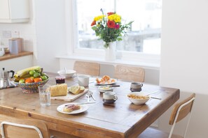 A dining table with various food items and drinks, a vase with flowers, and a window with a view of buildings. - The Salt House (Ilfracombe)