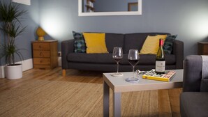 Una sala de estar con un sofá, dos copas de vino, una botella de vino y un libro sobre una mesa de centro.