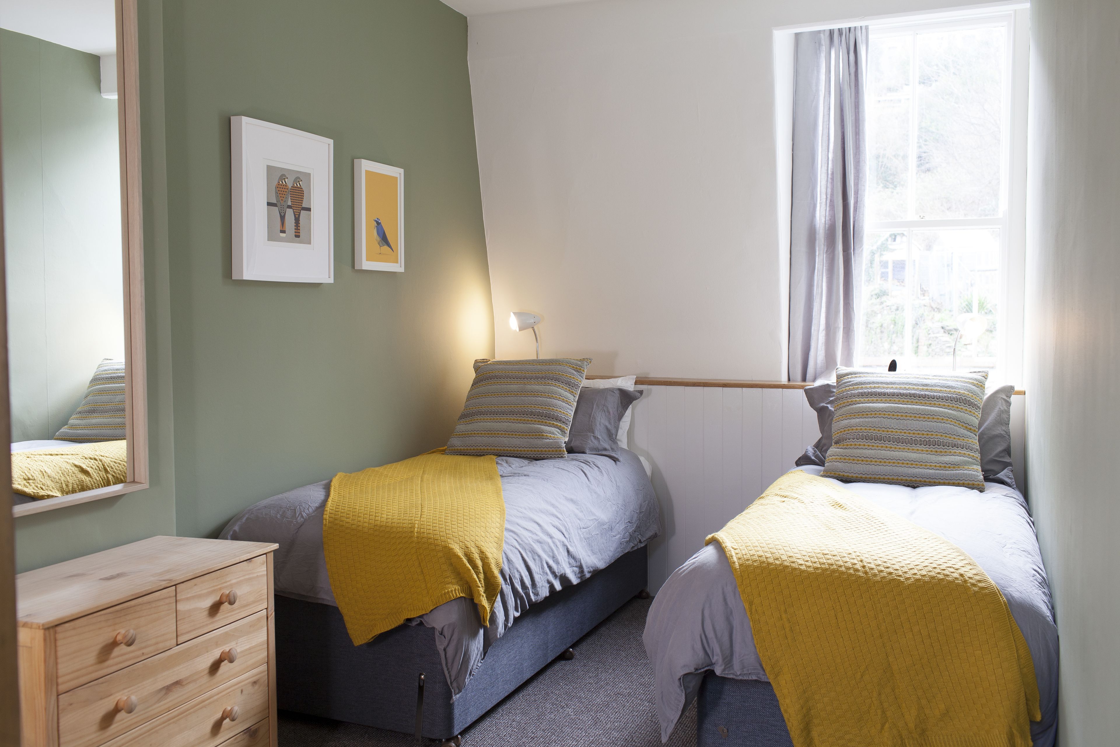 A bedroom with two beds, a dresser, and a window with curtains.
