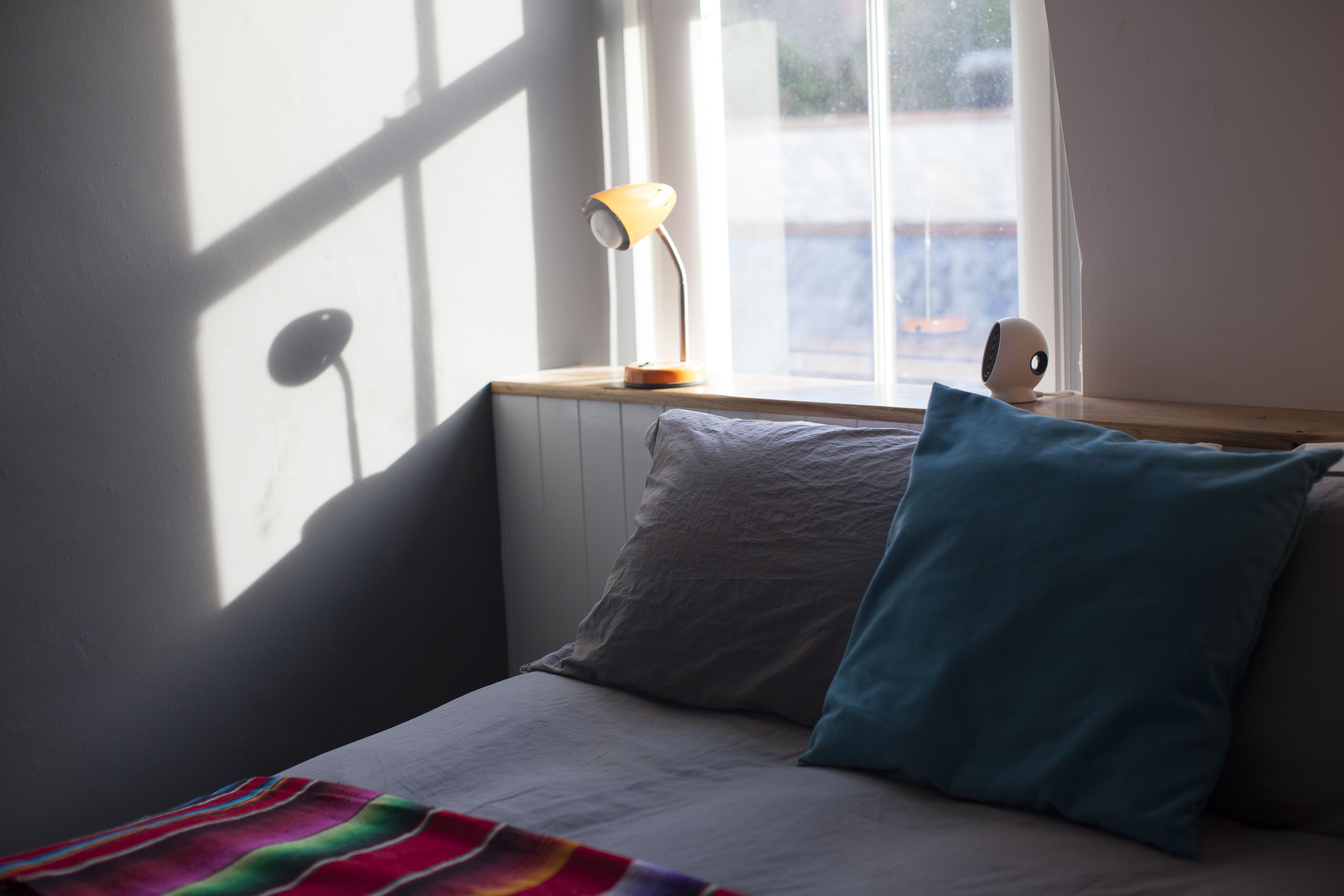 En seng med et farverigt tæppe, en lampe og en pude på et trænatbord.