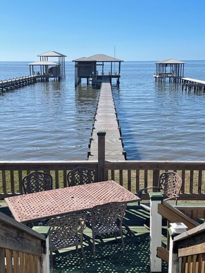 A wooden deck with a table and chairs, leading to a pier with two gazebos over the water. - Waterfront Home with Dock! (Fairhope)