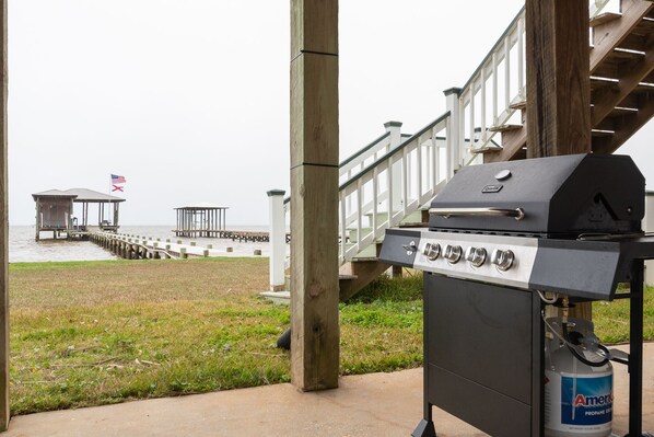 A barbecue grill with propane tank, wooden deck, and a pier extending into the water. - Waterfront Home with Dock! (Fairhope)
