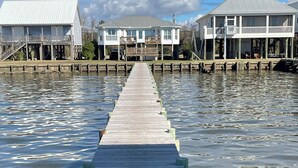 A wooden pier leading to a waterfront property with two white buildings, one with a balcony and the other with a covered deck. - Waterfront Home with Dock! (Fairhope)
