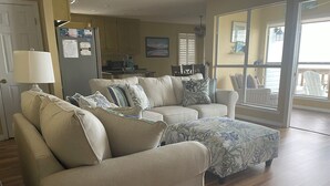 A living room with a beige sofa set, a patterned ottoman, and a dining area with a table and chairs. - Waterfront Home with Dock! (Fairhope)