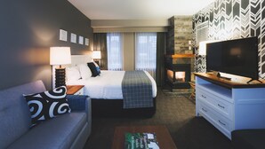 A hotel room with a bed, a sofa, a TV, a fireplace, and a wall with a geometric pattern.